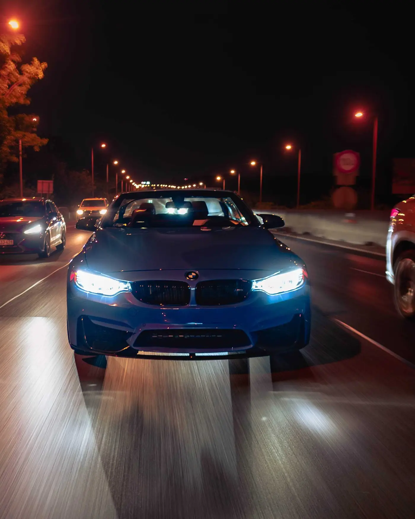 BMW M4 Convertible at night on a city road, street lights and traffic behind