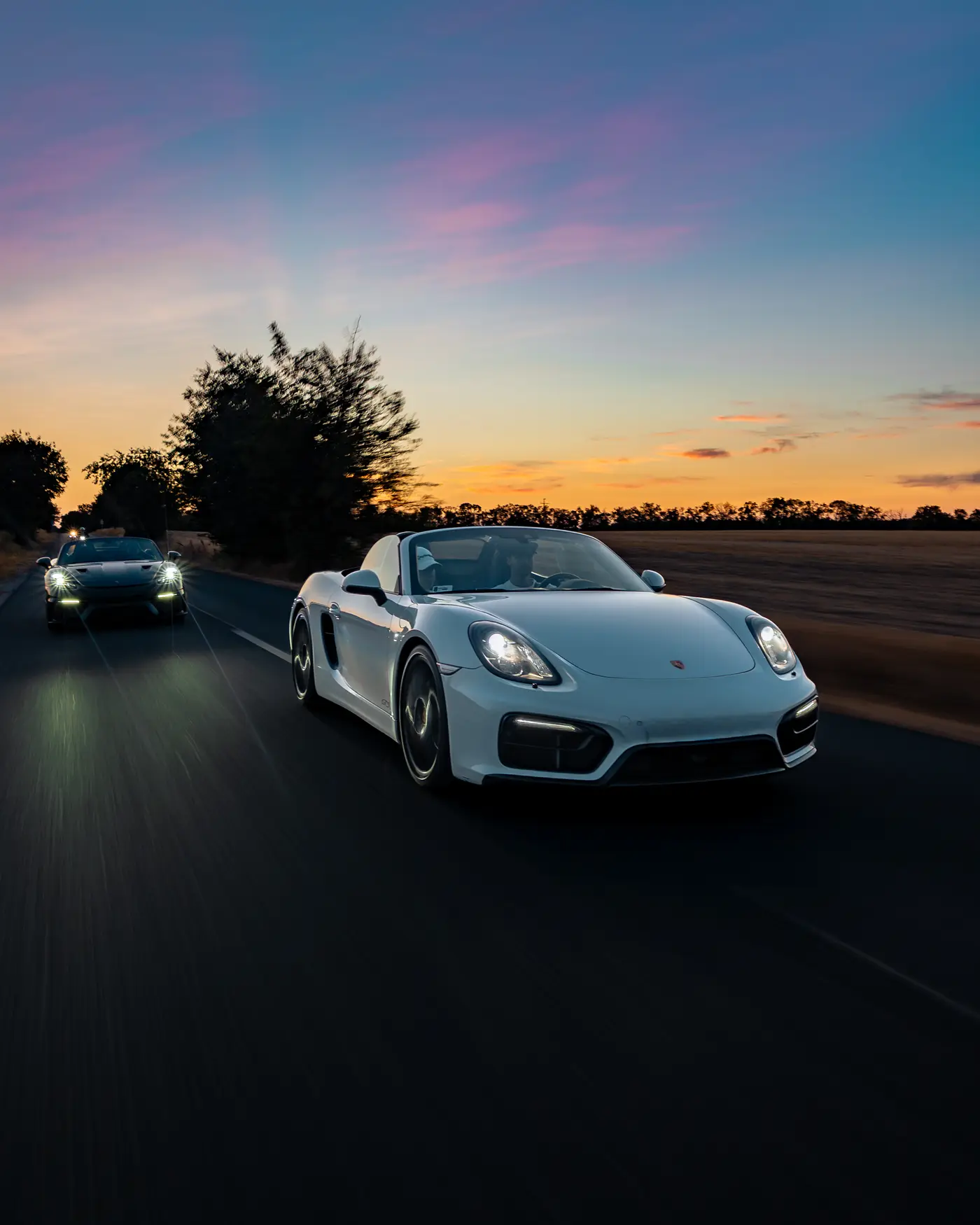 White Porsche Boxster GTS on an open road after sunset, a second car following
