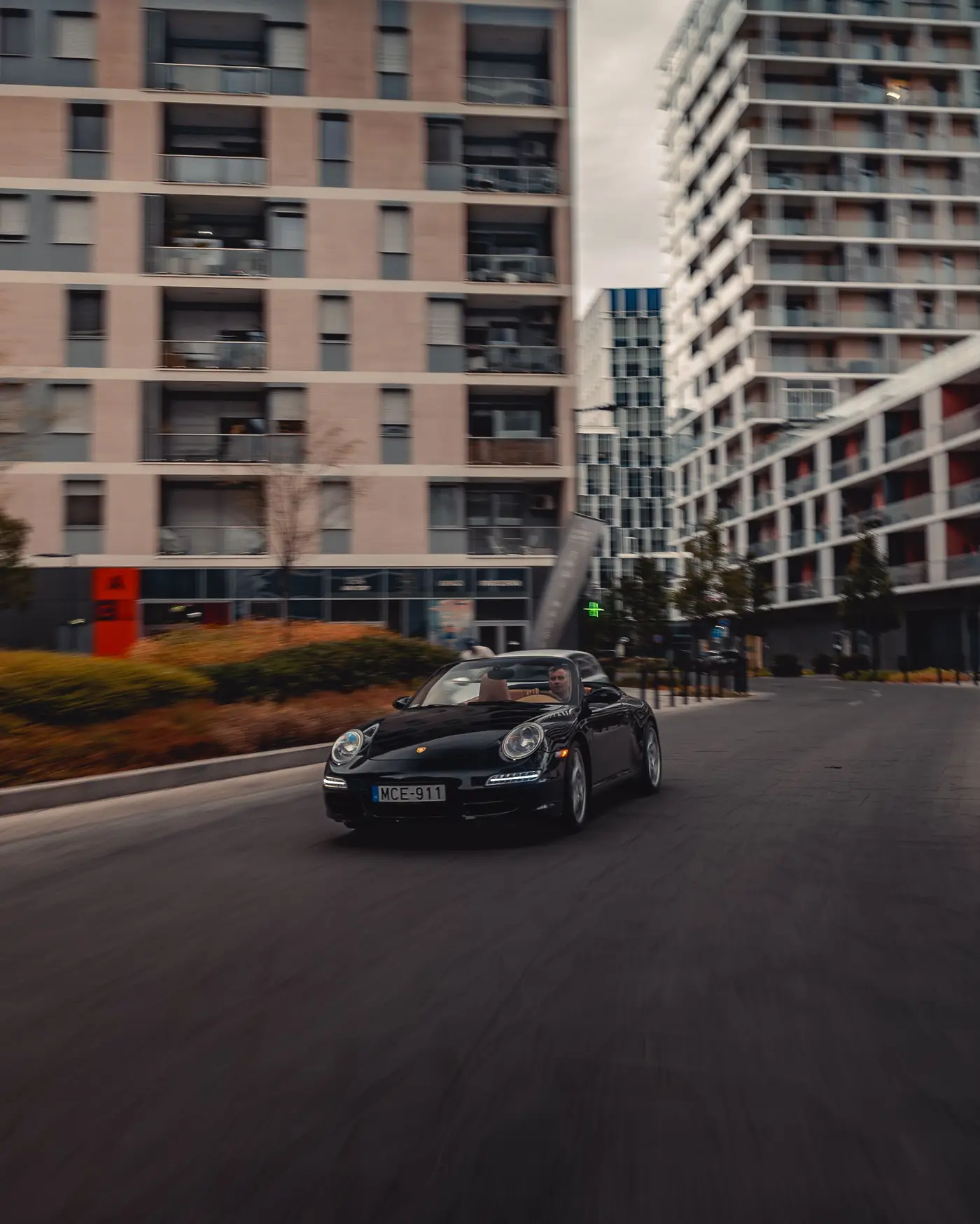 Black Porsche 911 Carrera Cabriolet on a new-build city street, apartment blocks behind