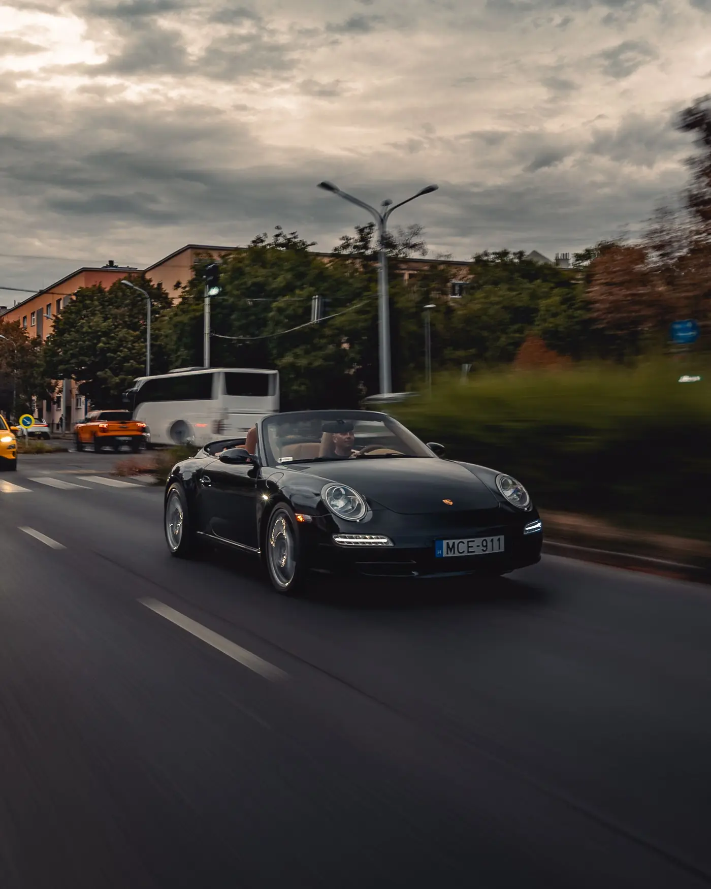 Porsche 911 Carrera Cabriolet on a city road under heavy clouds, a bus behind