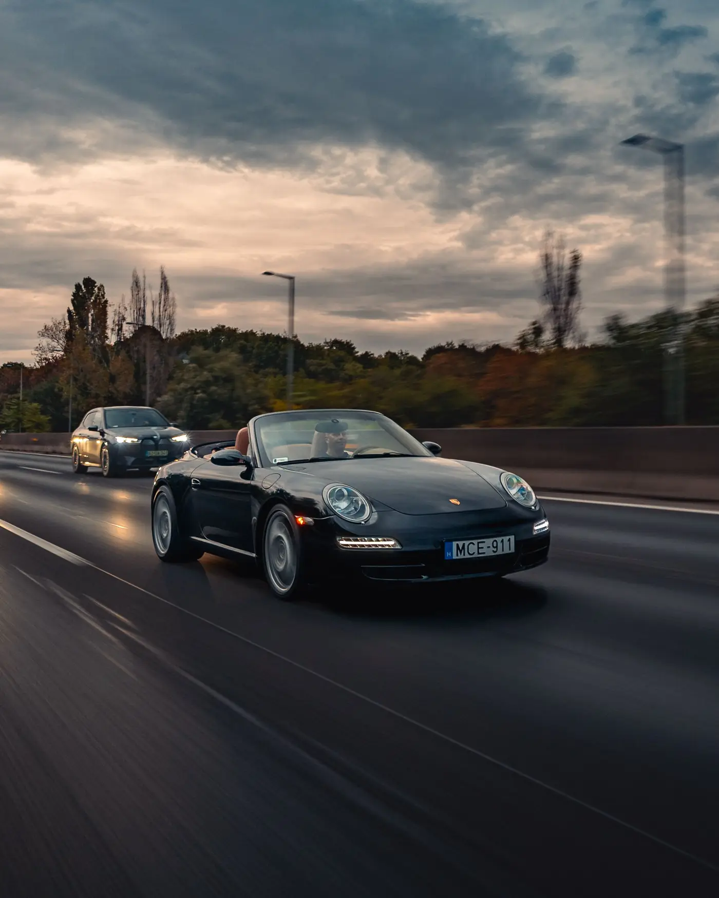 Porsche 911 Carrera Cabriolet at dusk, another car following, clouds lit by the setting sun
