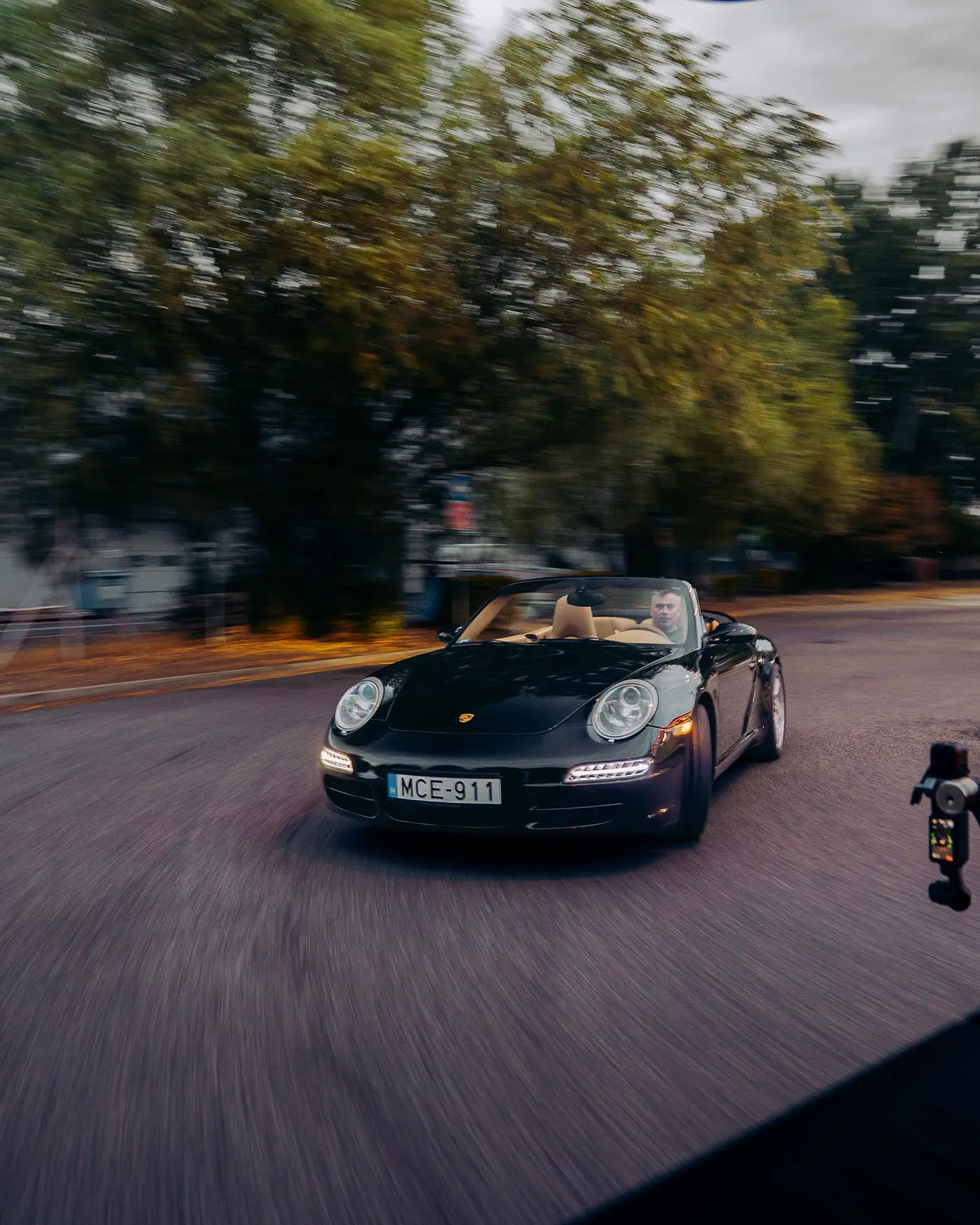 Porsche 911 Carrera Cabriolet seen from inside the camera car, trees blurred behind
