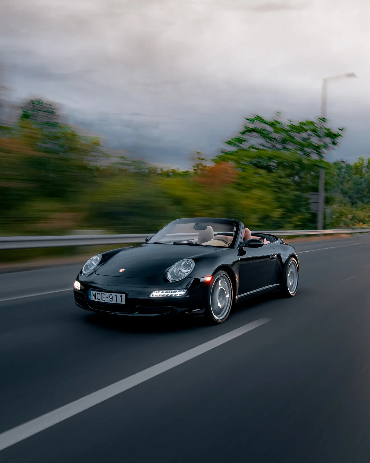 Black Porsche 911 Carrera Cabriolet, roof down, on a motorway with a blurred guardrail