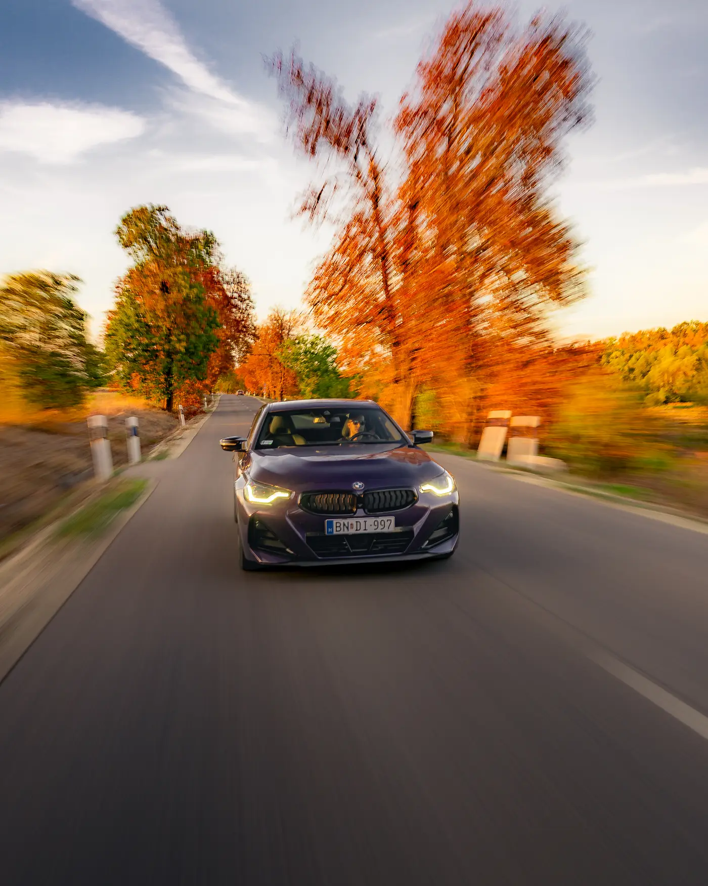 BMW M240i head-on on a country road, an orange autumn tree beside it