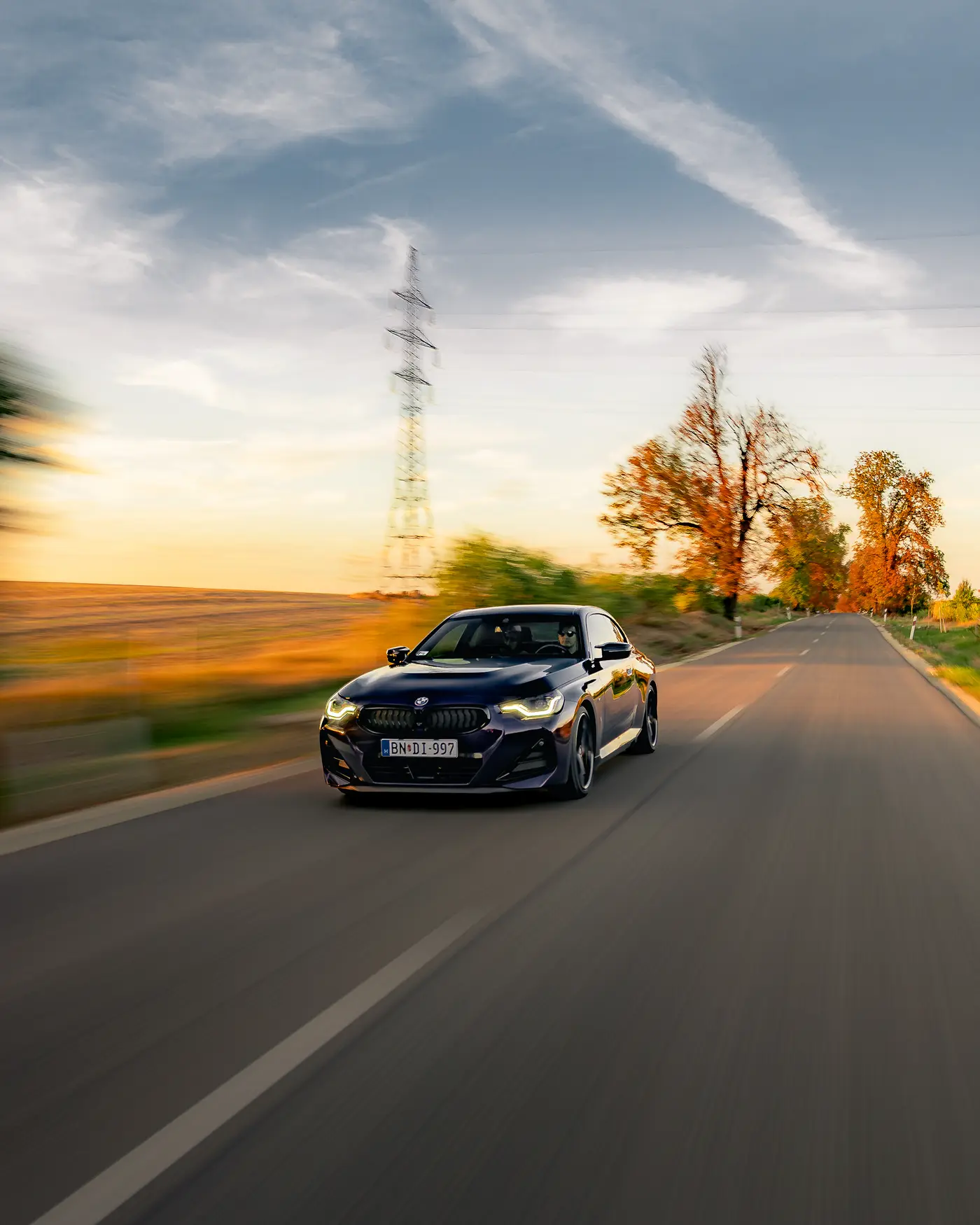 BMW M240i on an open country road, a pylon and autumn trees behind