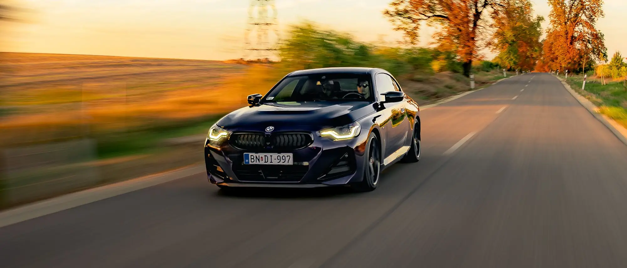 BMW M240i on an open country road, a pylon and autumn trees behind